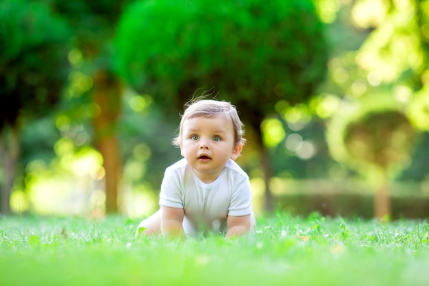 Ragazzo sveglio del bambino in tuta bianca che si siede sull'erba