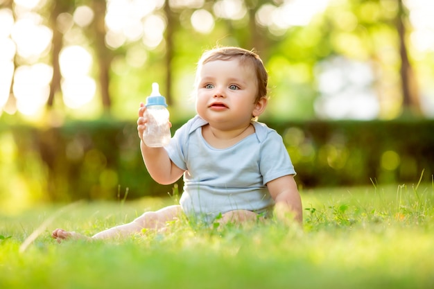 Ragazzo sveglio del bambino in tuta blu che si siede sull'erba