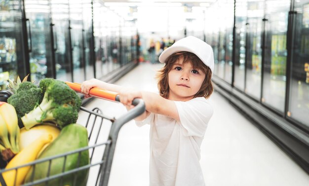 Ragazzo sveglio del bambino in un negozio di alimentari o in un supermercato che sceglie uno stile di vita sano di carote organiche fresche f