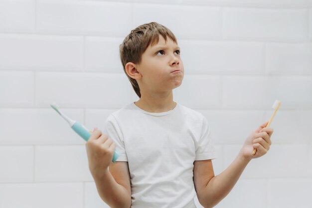 Ragazzo sveglio di 8 anni che tiene bambù e spazzolino da denti elettrico che fa la scelta