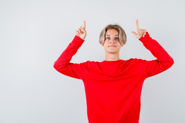 Ragazzo teenager che indica in su in maglione rosso e che sembra soddisfatto, vista frontale.