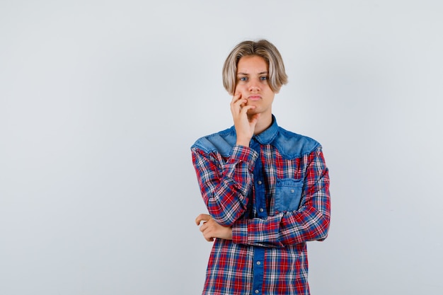 Ragazzo teenager con la mano sulla guancia in camicia a scacchi e sembra triste. vista frontale.