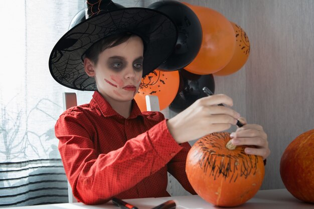 Ragazzo teenager felice in costume che prepara per la celebrazione di Halloween disegnando una zucca