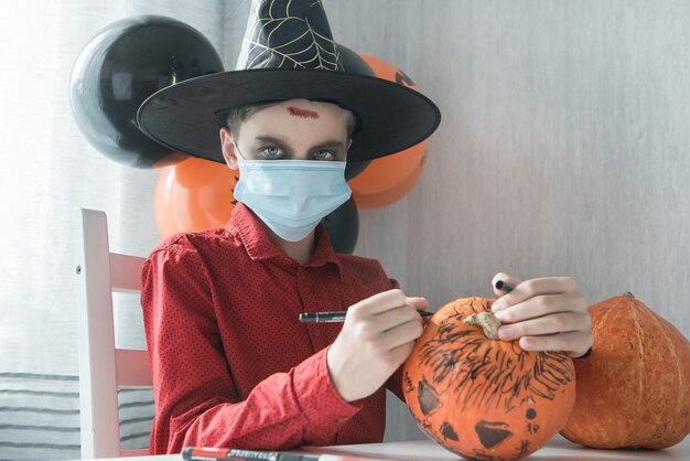 Ragazzo teenager in costume che prepara per la celebrazione di Halloween disegnando una zucca. Carnevale di Halloween con la nuova realtà con il concetto di pandemia
