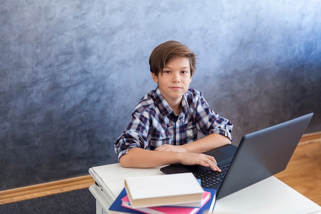 Ragazzo teenager sveglio di età che lavora al computer portatile a casa