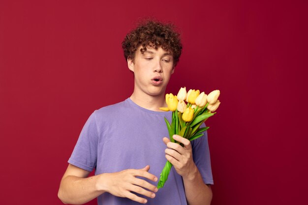 Ragazzo vizioso che tiene un mazzo di fiori gialli magliette viola sfondo rosso inalterato