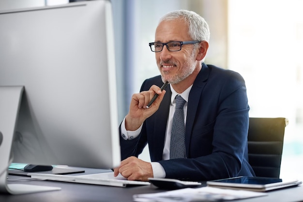 Raggiungere il successo alla vecchia maniera attraverso il duro lavoro Colpo di un uomo d'affari maturo sorridente che lavora alla sua scrivania in un ufficio