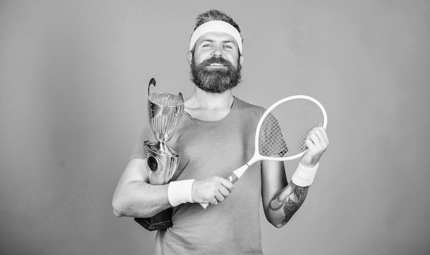 Raggiunto il massimo Giocatore di tennis vince il campionato L'atleta tiene la racchetta da tennis e il calice d'oro Vinci la partita di tennis L'uomo hipster con la barba indossa l'abbigliamento sportivo Successo e risultato Vincitore della partita di tennis