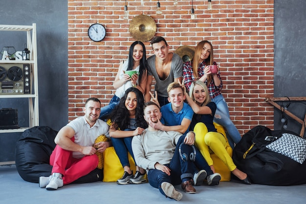 Raggruppi il ritratto dei ragazzi e delle ragazze multietnici con i vestiti alla moda variopinti che tengono l'amico che posa su un muro di mattoni, gente urbana di stile che si diverte, s circa lo stile di vita di insieme della gioventù