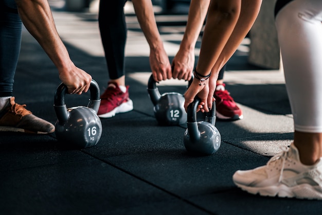 Raggruppi la gente in abiti sportivi che tengono i dumbbells durante l&#39;allenamento alla palestra, angolo basso, primo piano.