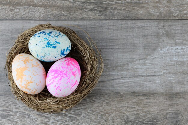 Raggruppi tre uova di Pasqua variopinte e decorate nel nido dell'uccello sulla tavola di legno d'annata. Immagine pubblicitaria Concetto di Pasqua o cibo con spazio libero.