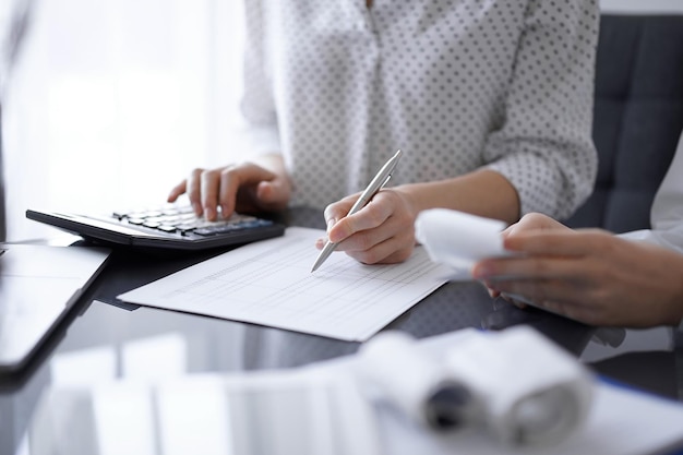 Ragioniere donna che utilizza una calcolatrice e un computer portatile mentre conta le tasse con un cliente o un collega. Squadra di controllo aziendale.