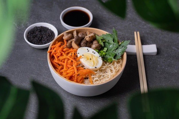 Ramen di zuppa di noodle in una ciotola bianca con funghi di carote all'uovo di pollo su uno sfondo di pietra ardesia scura