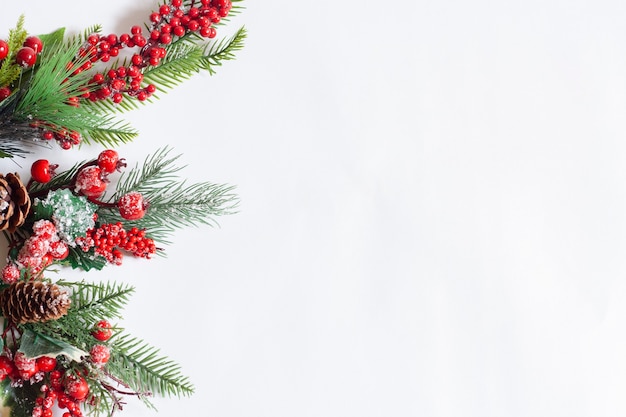 Rami dell'albero di Natale della carta con le bacche rosse su un fondo bianco, spazio della copia