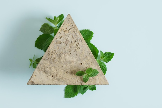 Rami e foglie di menta su una pietra triangolare, sfondo azzurro, pubblicità del tuo prodotto, prodotto naturale biologico con olio di menta, podio in cemento a forma di triangolo