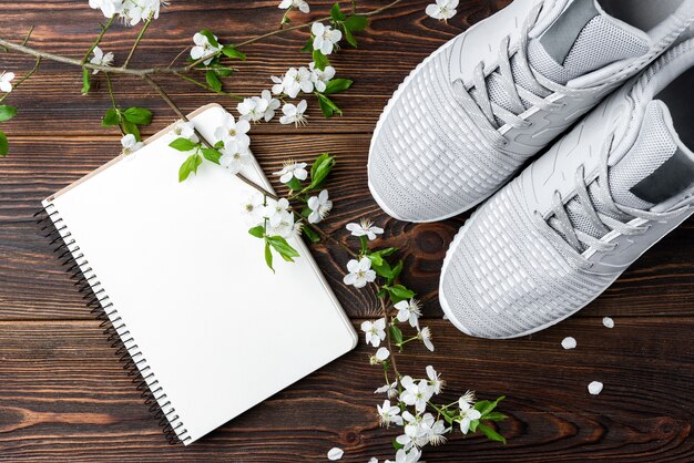 Ramo di fiori di primavera, scarpe da ginnastica e taccuino su fondo di legno scuro.