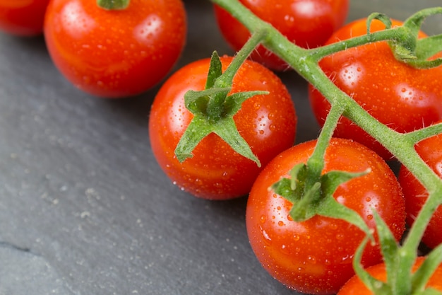 Ramo di piccoli pomodori rossi su sfondo di pietra nera da vicino