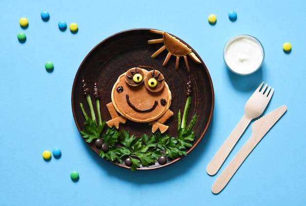 Rana divertente fatta di frittelle su un piatto, vista dall'alto. Colazione per bambini.