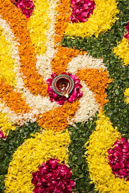 Rangoli di fiori per Diwali o Pongal realizzati con fiori di calendula o zendu e petali di rose rosse su sfondo bianco con lampada a olio di argilla al centro, messa a fuoco selettiva