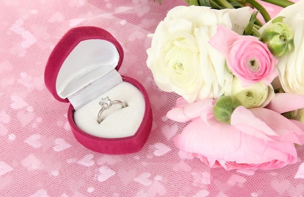 Ranuncoli (ranuncoli persiani) e anello di fidanzamento, su tela rosa