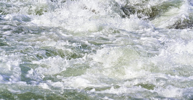 Rapido fiume primaverile che scorre sulle rocce in una giornata di sole, formando onde di acqua bianca, dettaglio del primo piano - sfondo astratto della natura.