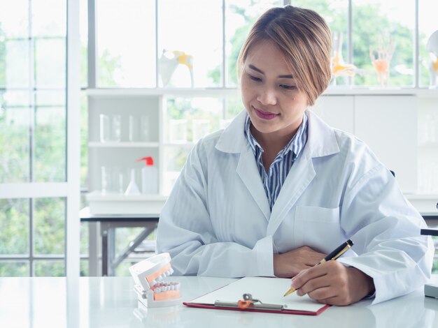 Rapporto di scrittura del dentista asiatico che lavora con il modello del dente