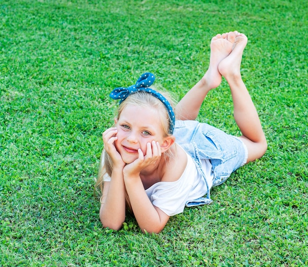 Ð¡rara bambina in una tuta di jeans, sdraiata su un prato verde