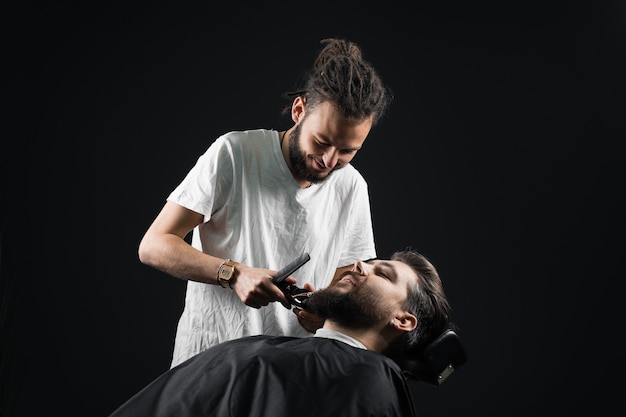 Rasatura della barba nel negozio di barbiere. Barbiere con i dreadlocks trim bell'uomo barbuto.