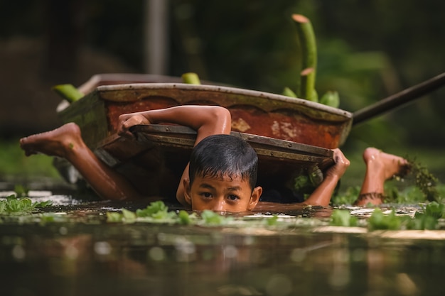 Ratchaburi, Tailandia - aprile 9,2019: Ragazzo che nuota nel cannal vicino al mercato di galleggiamento di Damnoen Saduak