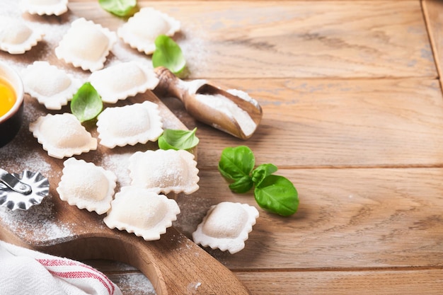 Ravioli Cibo italiano Gustosi ravioli di pasta fatta in casa con farina pomodori uova e verdure basilico su fondo in legno Processo di produzione dei ravioli italiani Sfondo degli ingredienti per la cottura degli alimenti Vista dall'alto