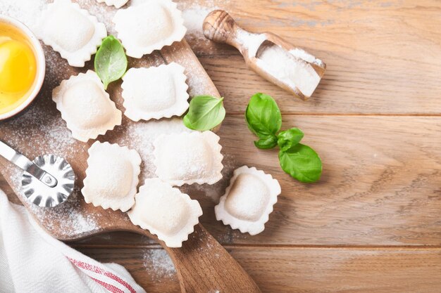 Ravioli Cibo italiano Gustosi ravioli di pasta fatta in casa con farina pomodori uova e verdure basilico su fondo in legno Processo di produzione dei ravioli italiani Sfondo degli ingredienti per la cottura degli alimenti Vista dall'alto