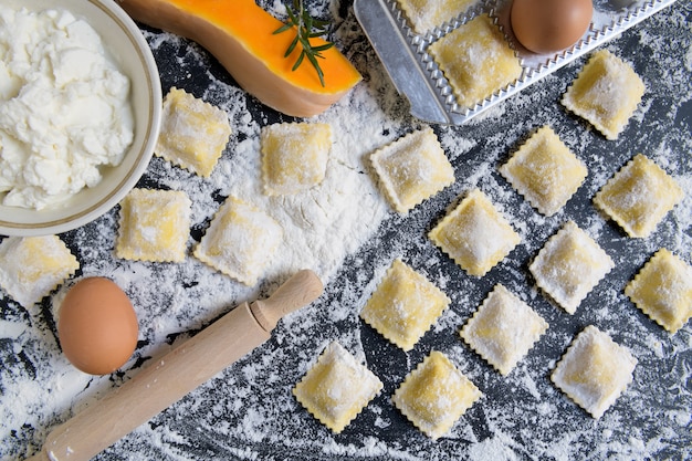 Ravioli crudi tradizionali con la zucca su una tavola di legno con farina, fatta a mano, processo di cottura