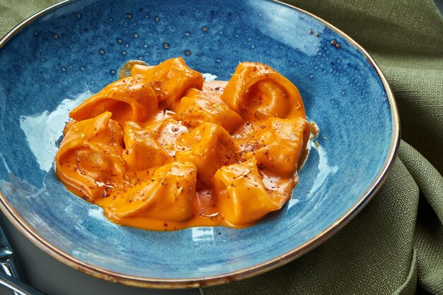 Ravioli d'arancia appetitosi in salsa con diversi ripieni (carne, pesce) in una ciotola blu su un tavolo di legno. Cucina italiana. Primo piano, messa a fuoco selettiva