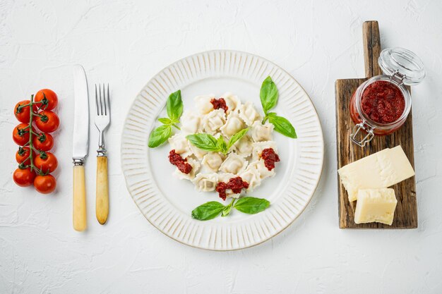 Ravioli di pasta con salsa di crema di funghi e formaggio - stile alimentare italiano impostato con basilico parmigiano e pomodoro sulla piastra bianca, su sfondo bianco, vista dall'alto laici piatta