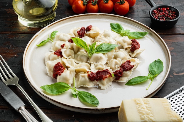 Ravioli di pasta con salsa di crema di funghi e formaggio - stile alimentare italiano impostato con basilico parmigiano e pomodoro sulla piastra bianca sul vecchio fondo della tavola in legno scuro