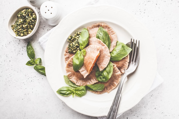 Ravioli di zucca con salsa al pesto in un piatto bianco.