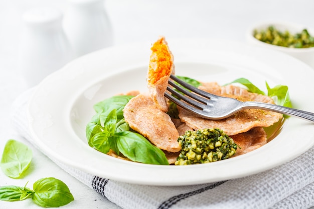 Ravioli di zucca con salsa al pesto in un piatto bianco.