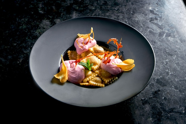 Ravioli dolci con ciliegie e gelato rosa serviti in un piatto nero su un tavolo di marmo scuro. Cibo del ristorante. Cucina italiana. Gnocchi con ripieno dolce