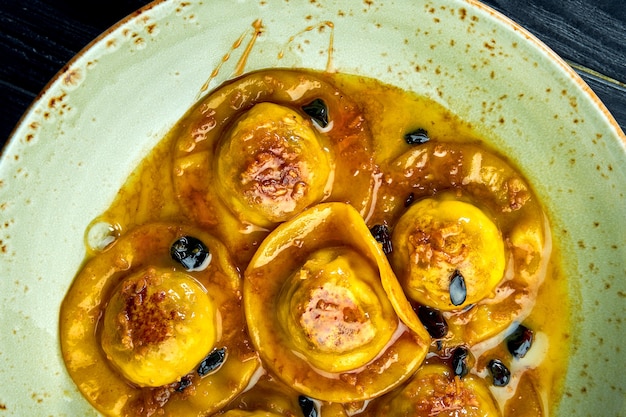 Ravioli fatti in casa e appetitosi con petto d'anatra e mirtilli rossi, serviti con salsa in un piatto blu su una superficie di legno scuro. Piatto della cucina italiana