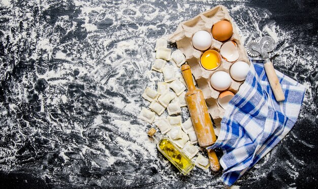 Ravioli freschi al mattarello, uova e olio d'oliva. Sulla tavola nera con farina. Vista dall'alto