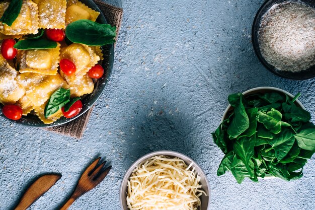 Ravioli freschi ripieni di spinaci, con ingredienti su un tavolo di legno. Cibo italiano fatto in casa