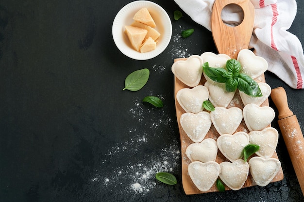 Ravioli italiani a forma di cuore Gustosi ravioli crudi con farina e basilico su sfondo scuro Sfondo di ingredienti per la cottura degli alimenti Idee per il pranzo di San Valentino o festa della mamma Vista dall'alto con spazio per la copia