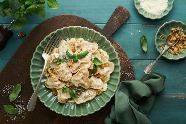 Ravioli italiani fatti in casa a forma di cuore con salsa di formaggio e carne di manzo, cipolle caramellate, basilico e zafferano su sfondo blu in legno vecchio Sfondo degli ingredienti del menu di cottura degli alimenti Vista dall'alto