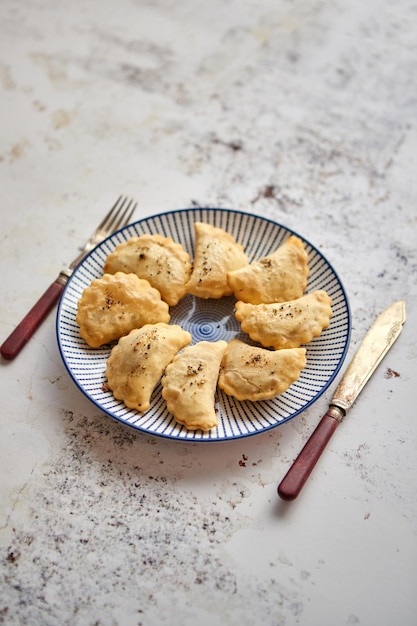 Ravioli polacchi fritti caldi e gustosi con ripieno di carne cosparso di pepe fresco Posizionati su un piatto di ceramica blu Vista dall'alto su sfondo bianco arrugginito con spazio per la copia