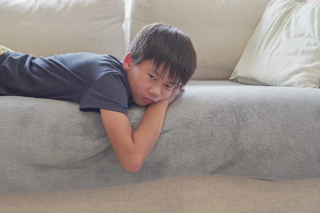Razza mista ragazzo asiatico preteen sentirsi annoiato sdraiato sul divano di casa, distanza sociale, quarantena, concetto di isolamento, consapevolezza dell'autismo, salute mentale