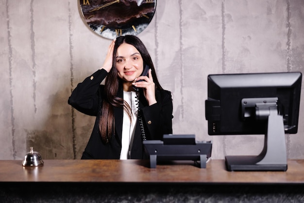 Receptionist dell'hotel Reception moderna dell'hotel con campanello Lavoratrice receptionist femminile felice in piedi al bancone dell'hotel e parlando al telefono