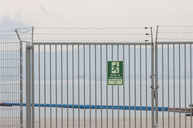 Recinzione con filo spinato vicino alla riva del mare e segnale di uscita di emergenza su di essa