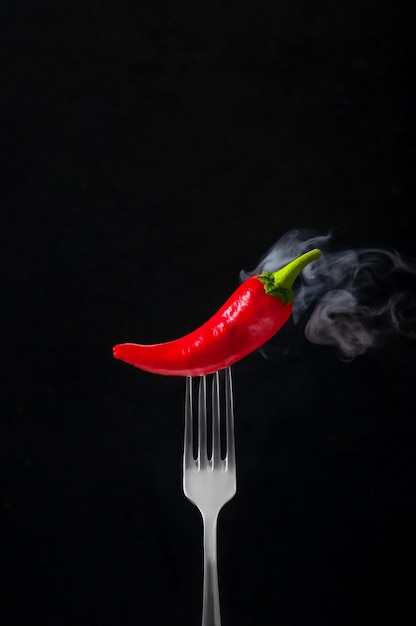 Red Hot Chili Pepper sulla forcella con fumo su sfondo nero.