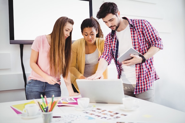 Redattori che utilizzano computer portatile e compressa digitale all'ufficio creativo