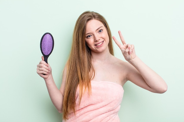 Redhair donna sorridente e guardando felice gesturing vittoria o pace concetto pettine per capelli